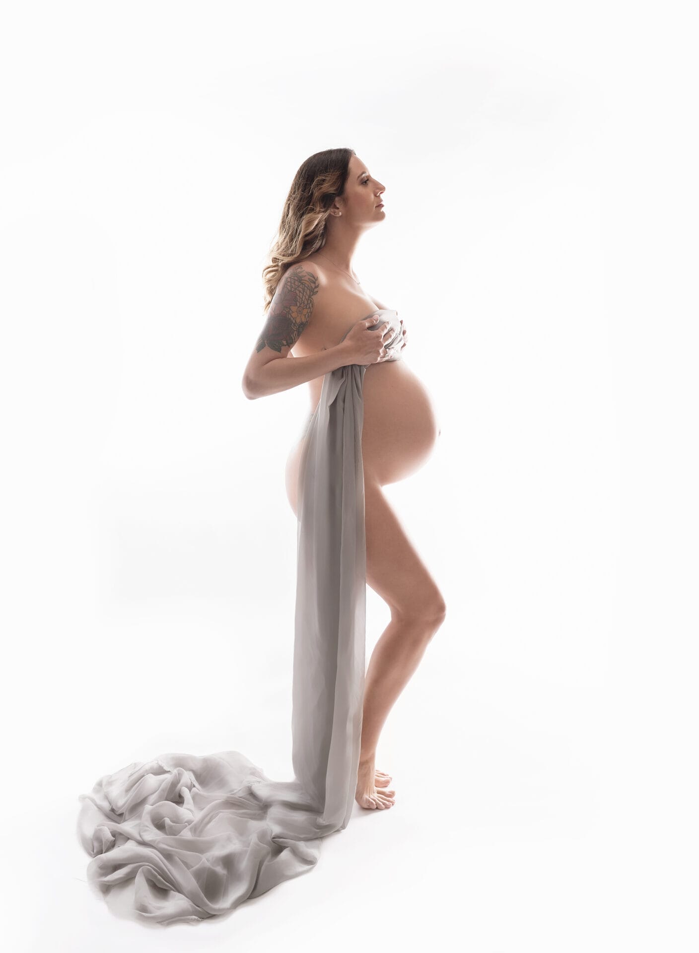 A pregnant mom in the studio with fabric draped around her body and her pregnant belly exposed. 