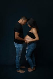 expecting young couple in black shirt and jeans embracing baby belly having fun in Baton Rouge before baby arrives