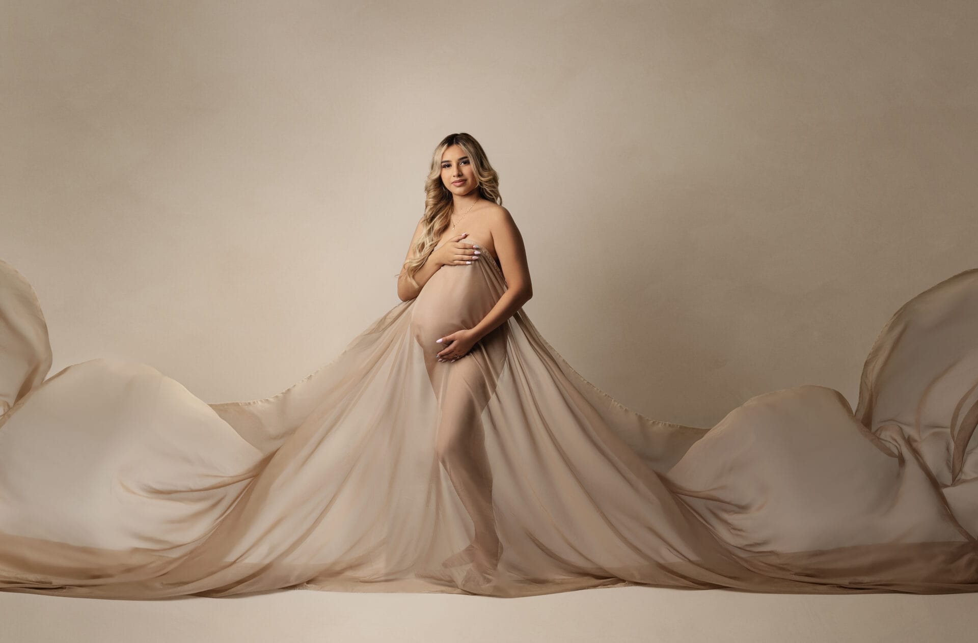 An expectant mom in the studio with beige fabric draped over her body at Lafayette birthing center.
