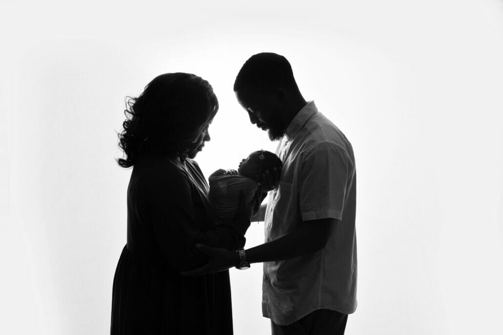 Two parents holding a newborn are silhouetted against a studio backdrop with Lafayette newborn photographer.