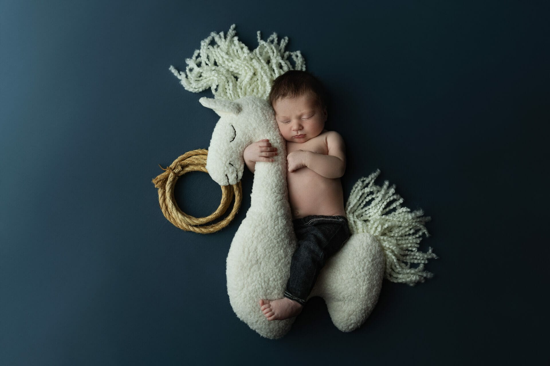 A newborn baby boy with jeans on a blue back drop on a horse