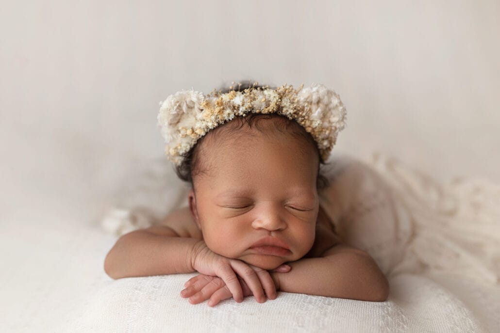 Baby girl sleeping with chin on hands-on ivory lace backdrop with a floral bear halo.
