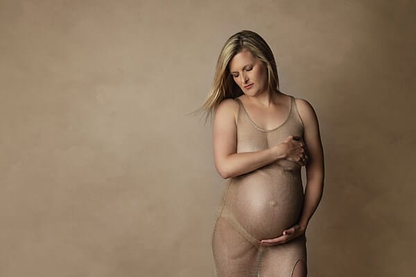 Mother-to-be with beige see-through dress caressing belly.
