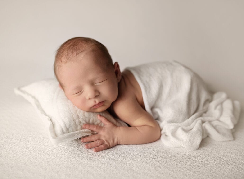 Photo of a baby boy laying on a cream backdrop with his head resting on a pillow with New Orleans newborn photographer