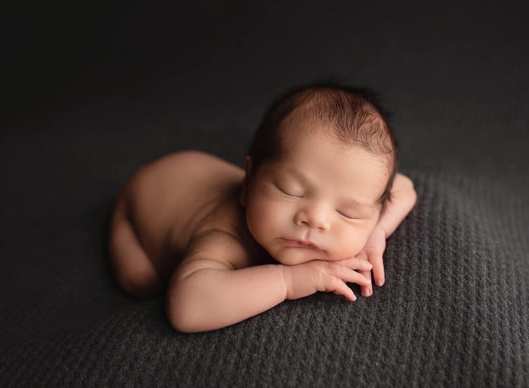 Baby boy lying on tummy with chin resting on hands-on a grey backdrop.