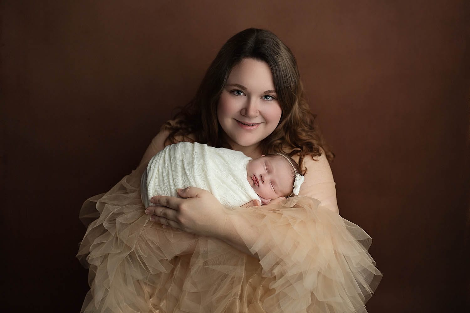 A new mother in a tan tule dress cradles her sleeping newborn baby girl in her arms thanks to lactation consultant new orleans