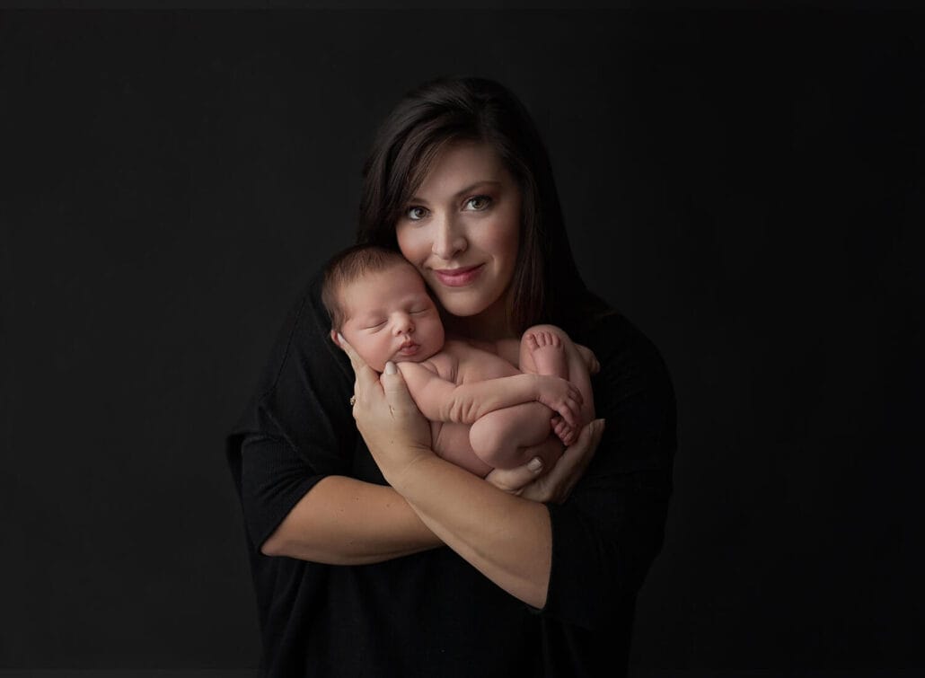 A happy new mother cradles her sleeping newborn baby while standing in a studio after meeting new orleans nannies