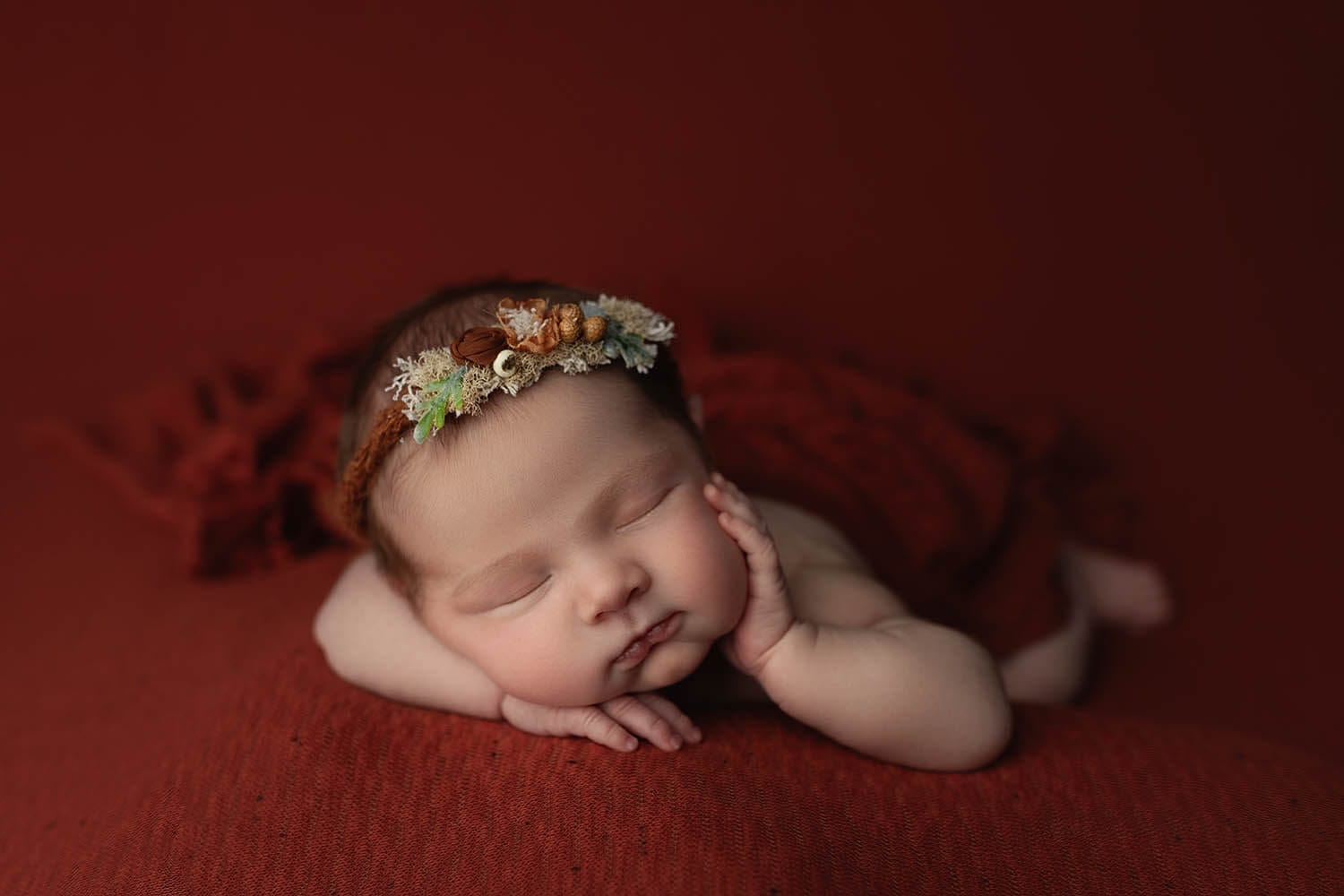 A sleeping newborn baby lays on her stomach with a hand on her cheek and a floral headband after meeting new orleans pediatricians