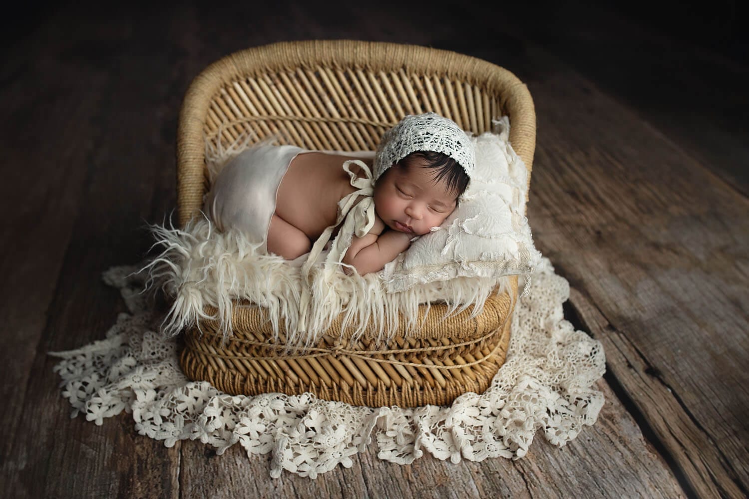 A newborn baby sleeps in a wicker bench on a pillow and fur blanket in a studio after meeting new orleans pediatricians
