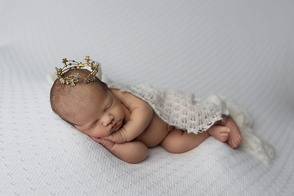 A newborn baby sleeps under a lace blanket wearing a tiny crown before visiting pediatric dentist new orleans