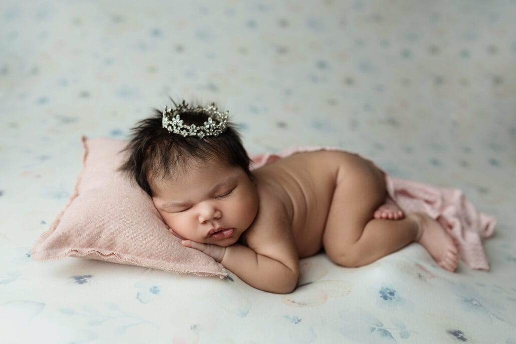 A newborn baby princess sleeps on a bed in a tiny crown before meeting a pediatric dentist new orleans