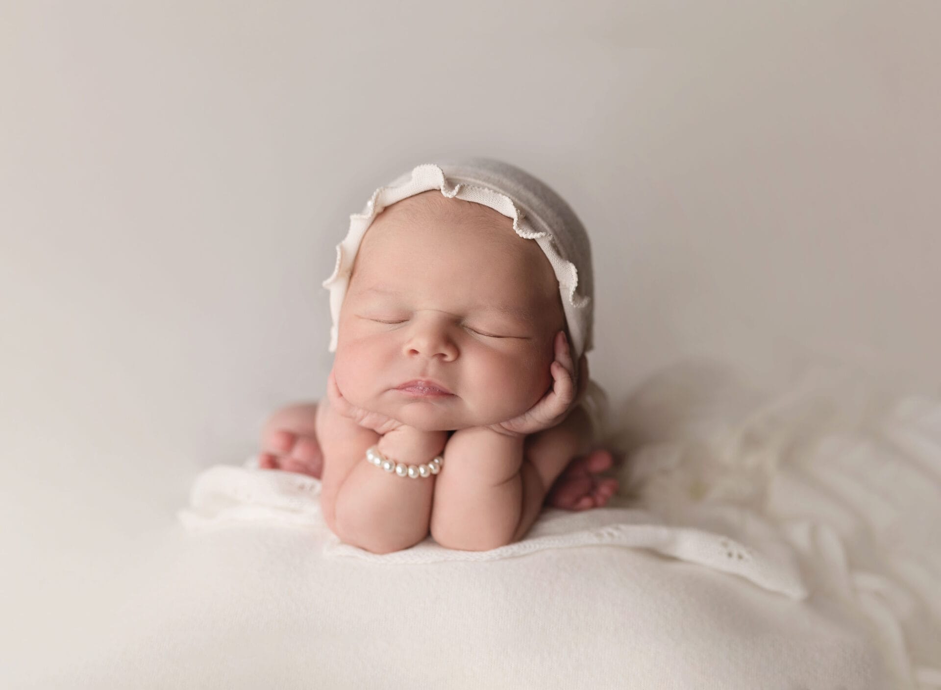 A newborn girl in the studio in a froggy pose with a pearl bracelet at Baton Rouge prenatal chiropractor.