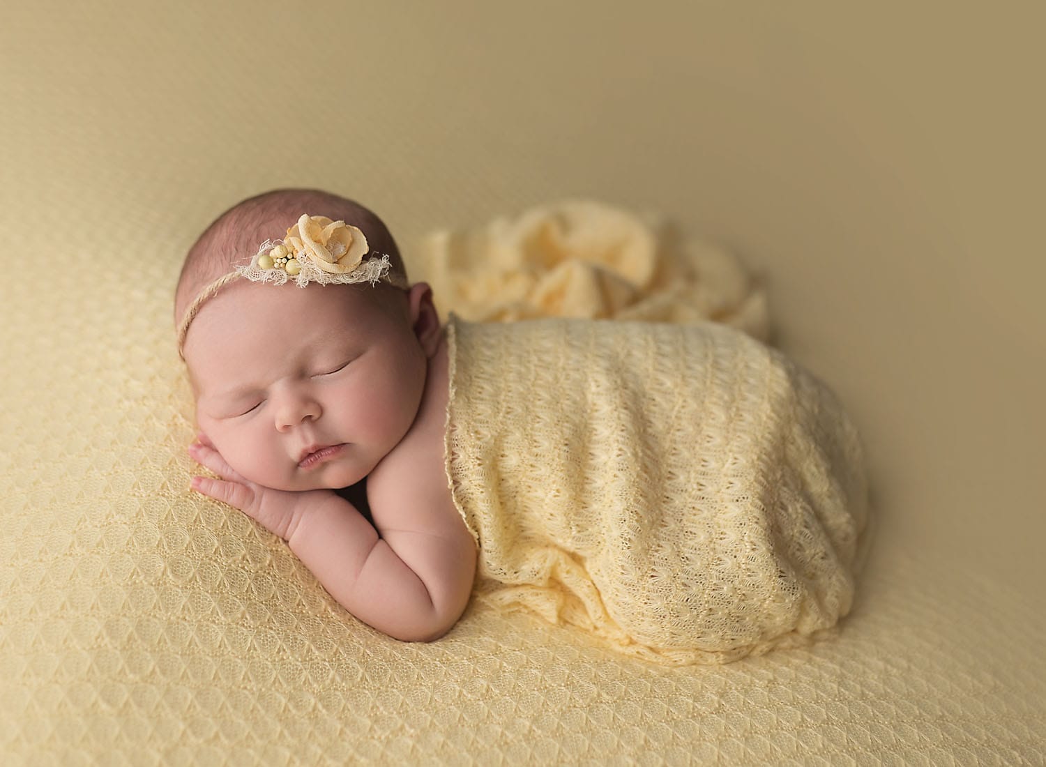 A baby girl laying on a yellow backdrop with her tiny hand under her cheek with a yellow wrap draped over her back.