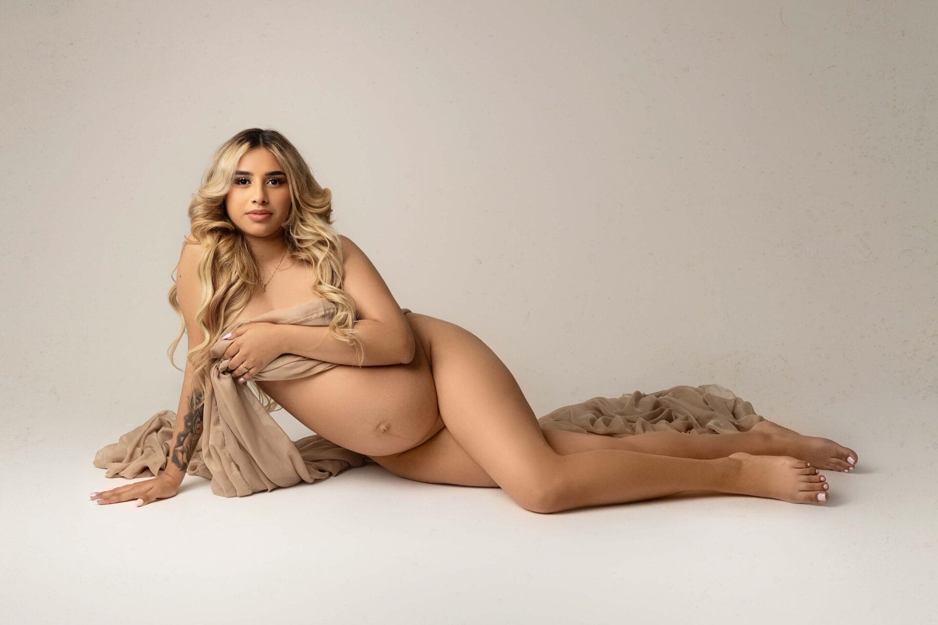 A pregnant mom-to-be in the studio posed on the floor with fabric over her chest and a pregnant belly exposed with Baton Rouge water birth.