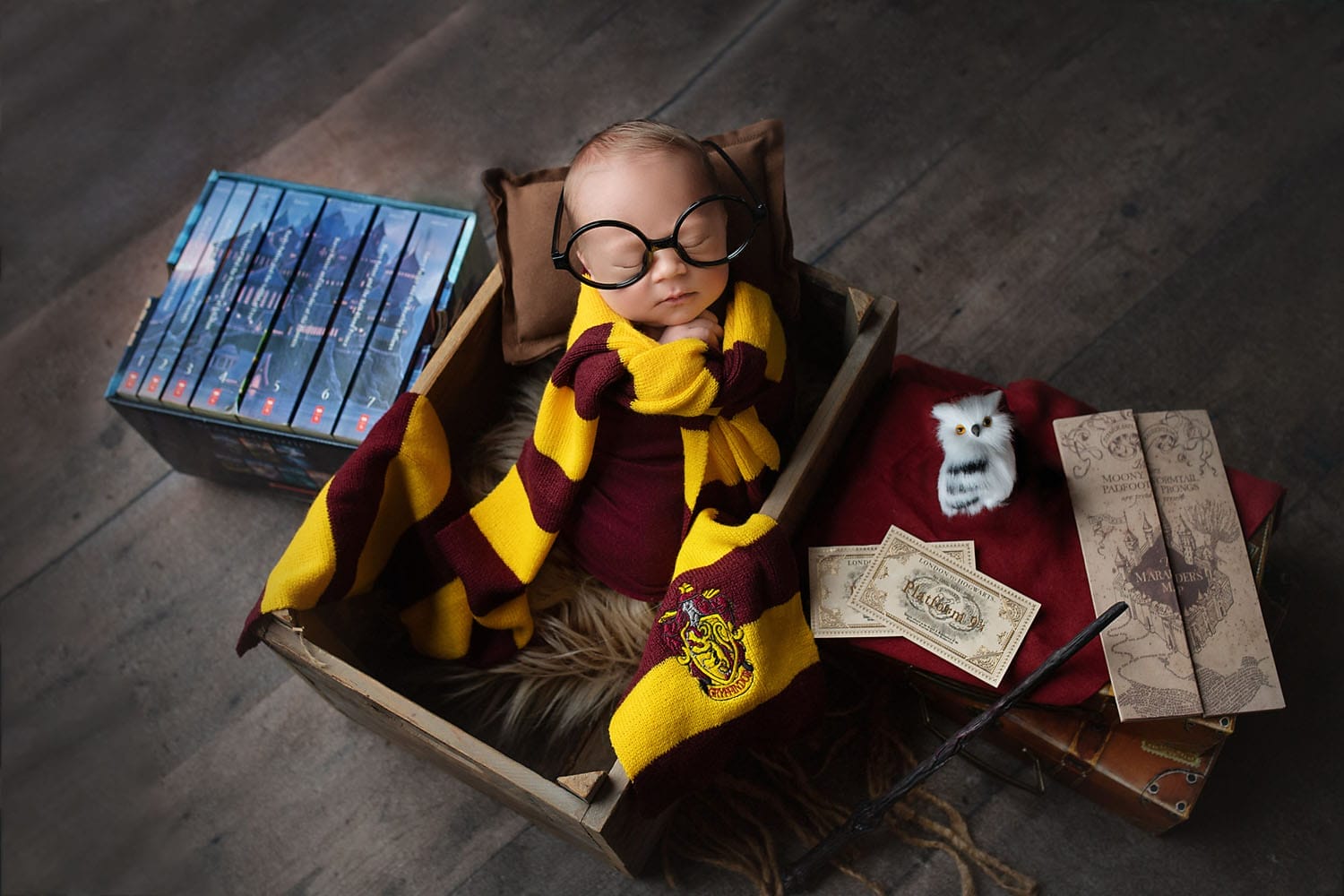 A newborn in the studio with a set up of Harry Potter with the newborn wearing glasses with a Harry Potter scarf at a New Orleans prenatal chiropractic clinic.
