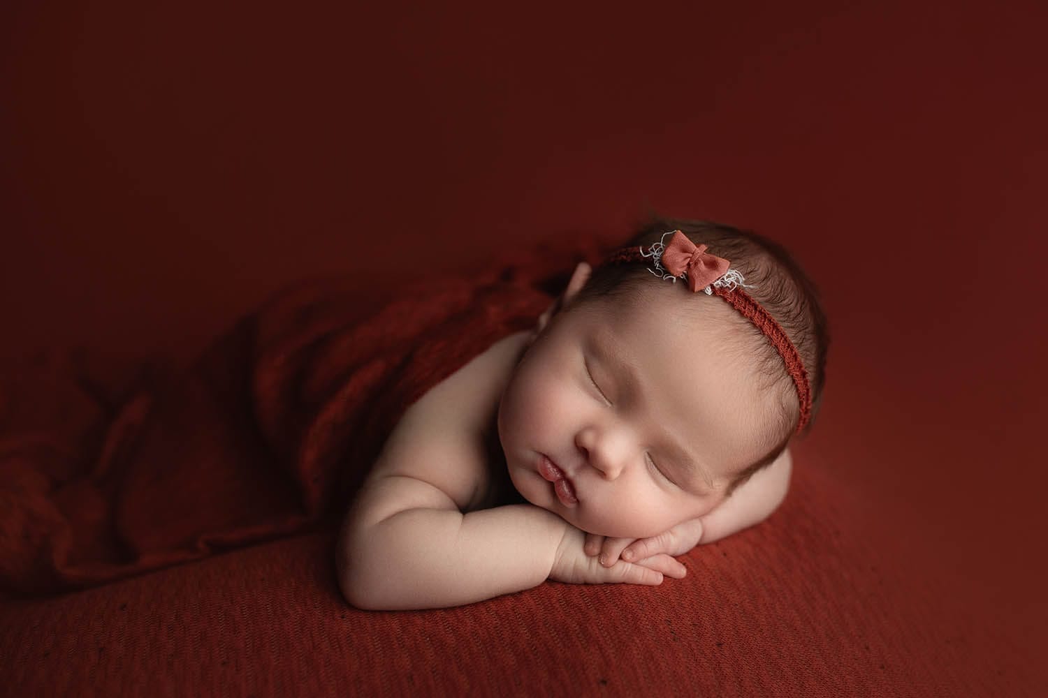 A newborn baby girl in the studio on her tummy posed with her cheeks on her hands with a floral headband at Lafayette prenatal chiropractor.