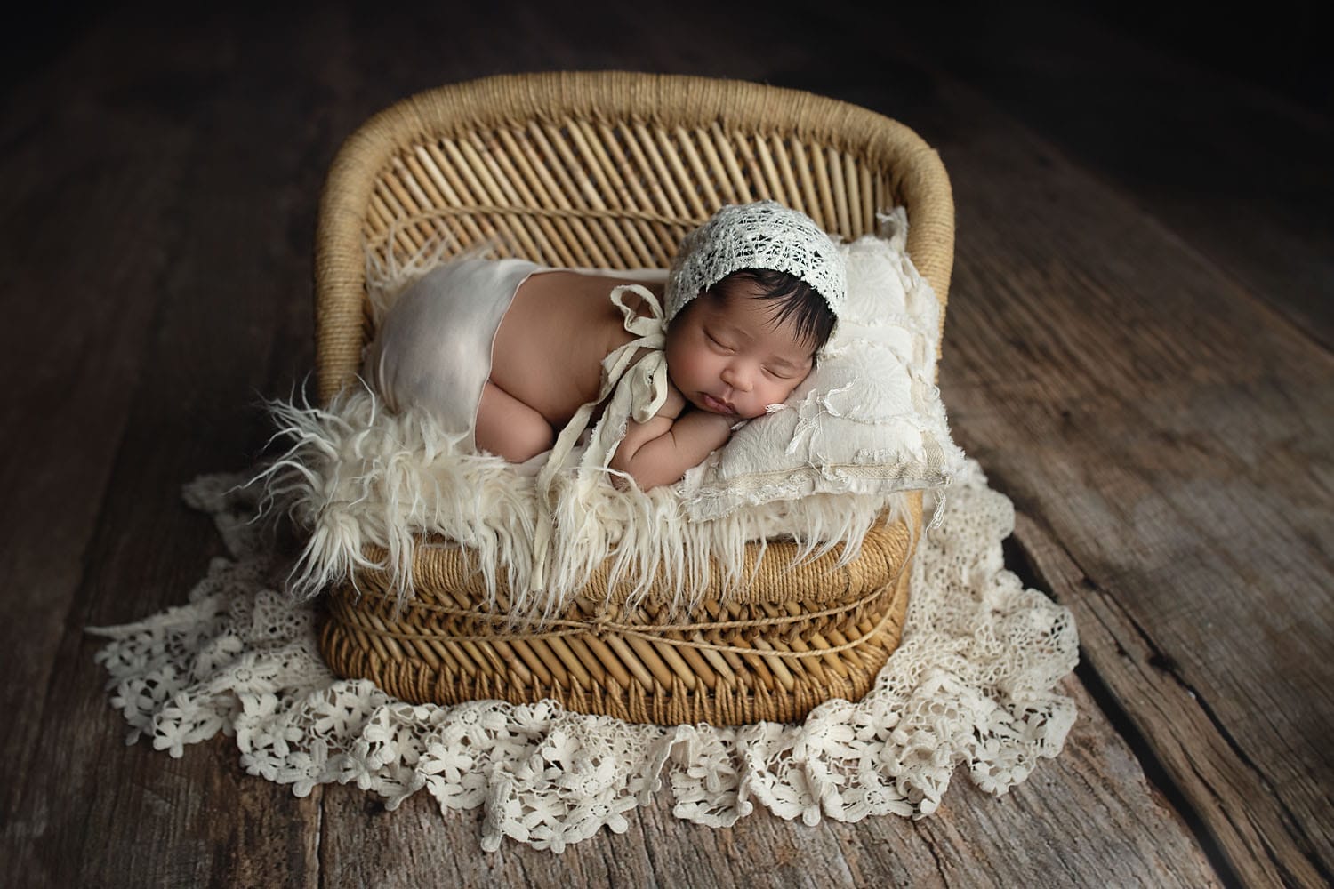 A newborn baby girl in the studio posed on her tummy on a bed with lace fabric layers. 