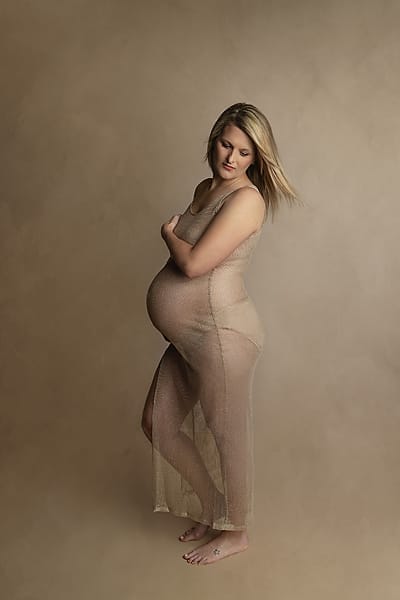 A pregnant mom is to be in the studio wearing a sheer beige dress and embracing her pregnant body. 