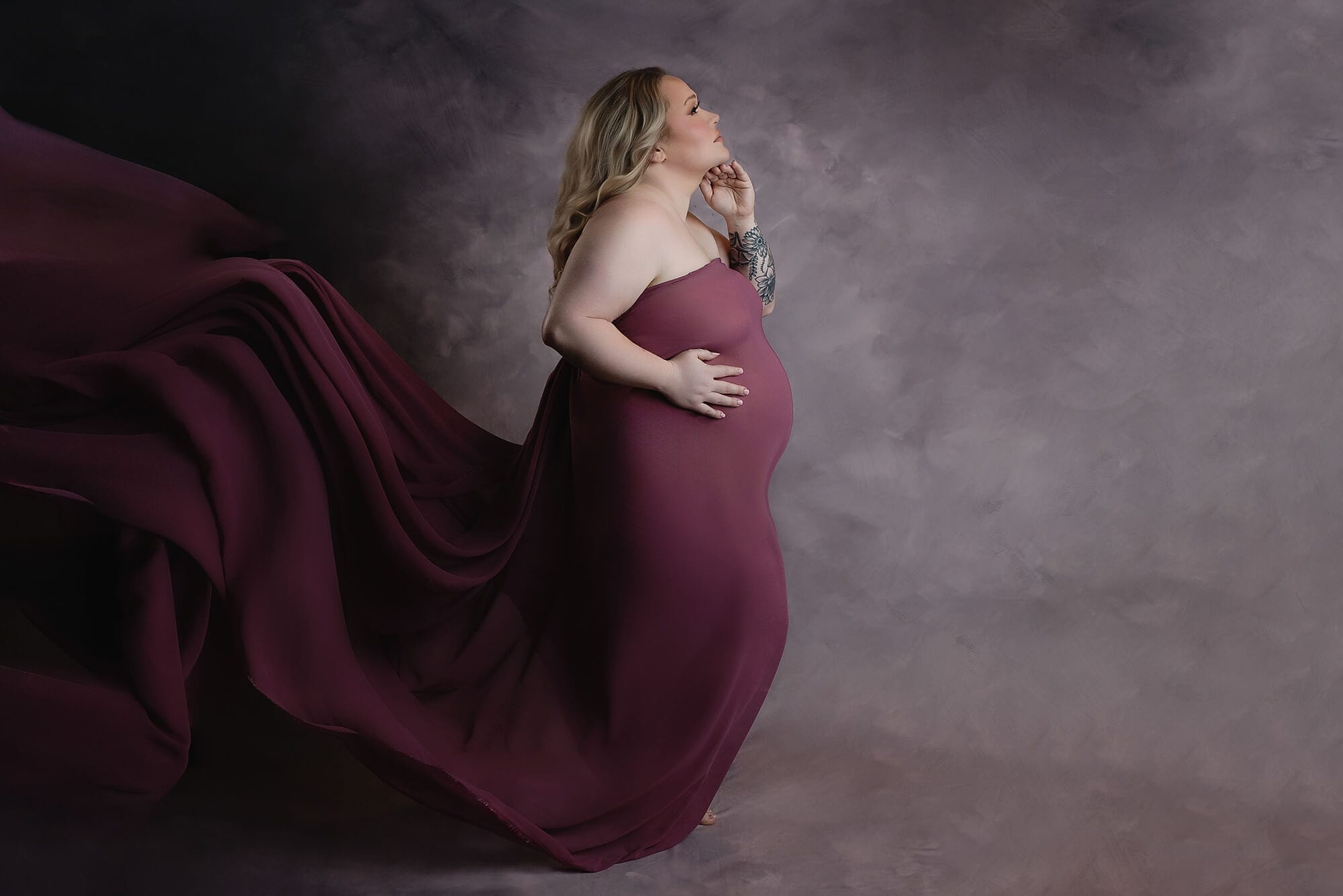 A soon to be mom in the studio with purple fabric draped over her pregnant body.