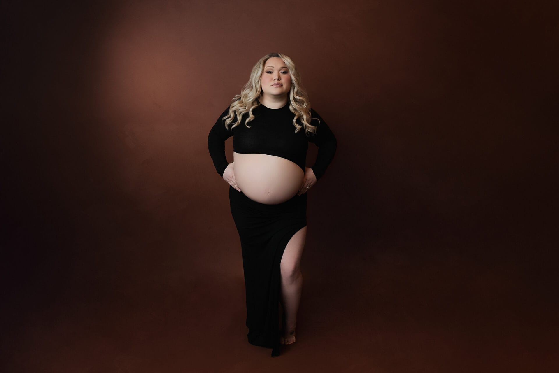 A pregnant mom in the studio with a black gown and elegantly standing with her hands on her hips at a New Orleans prenatal yoga studio.