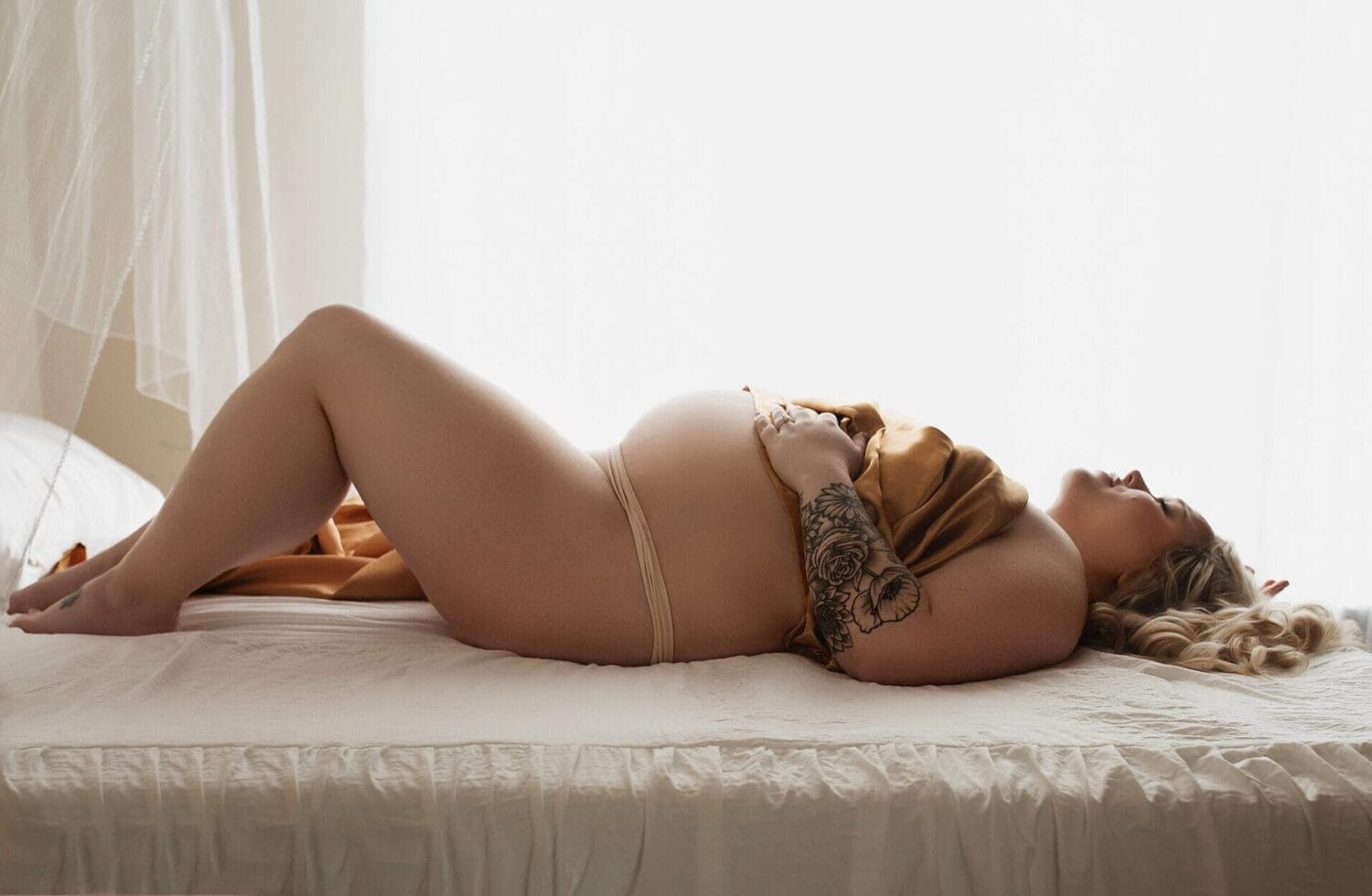 Pregnant mom in the studio lying on the bed with belly exposed.