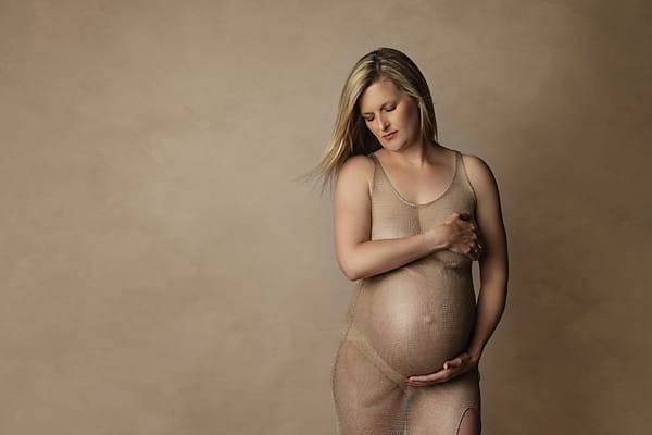 An expectant mom in the studio with beige dress caresses her belly.