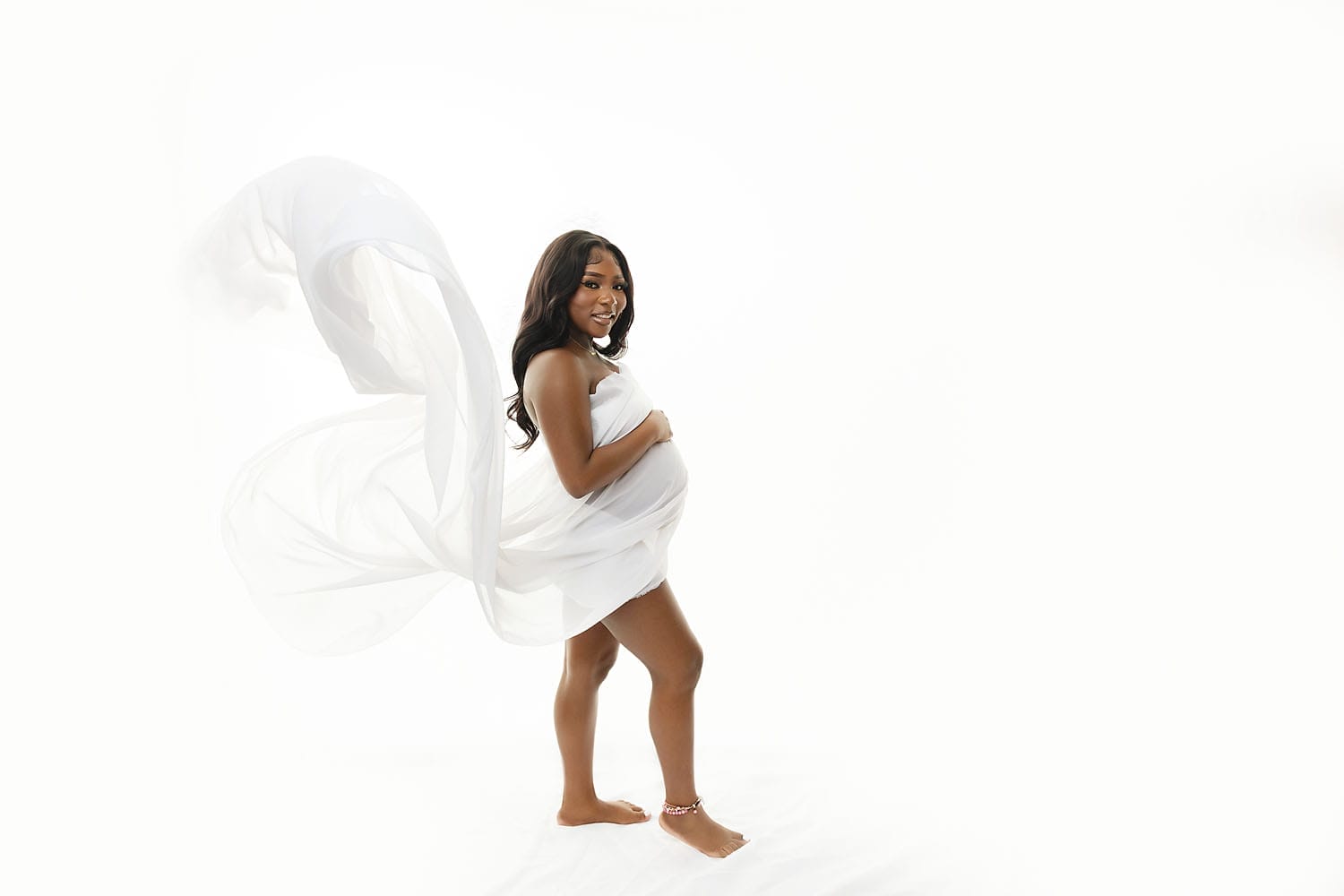 A pregnant mom to be in the studio with white flowing fabric.
