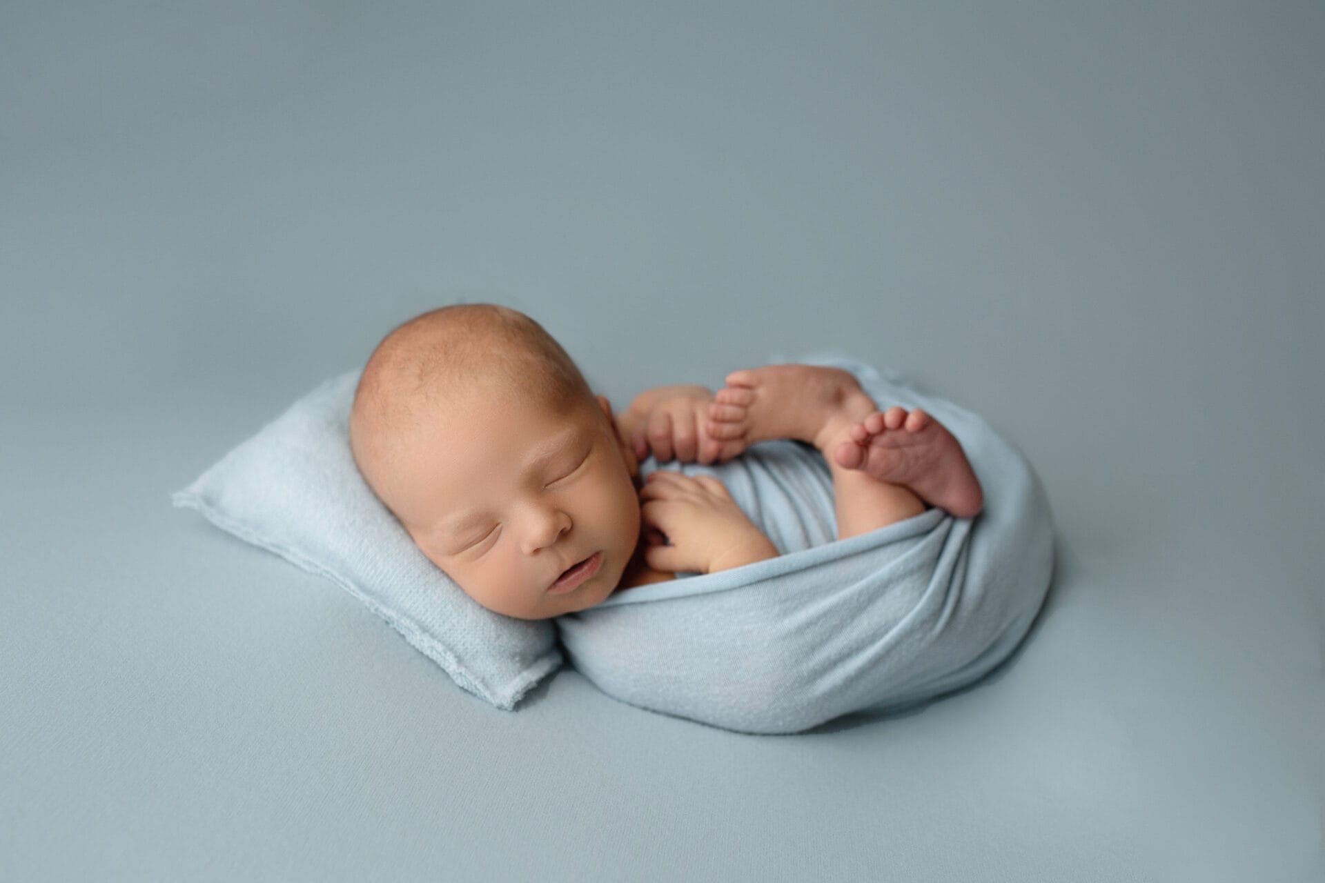 A Baton Rouge newborn in the studio with Melinda Gilmore Photography on a baby blue backdrop wrapped in a womb pose.